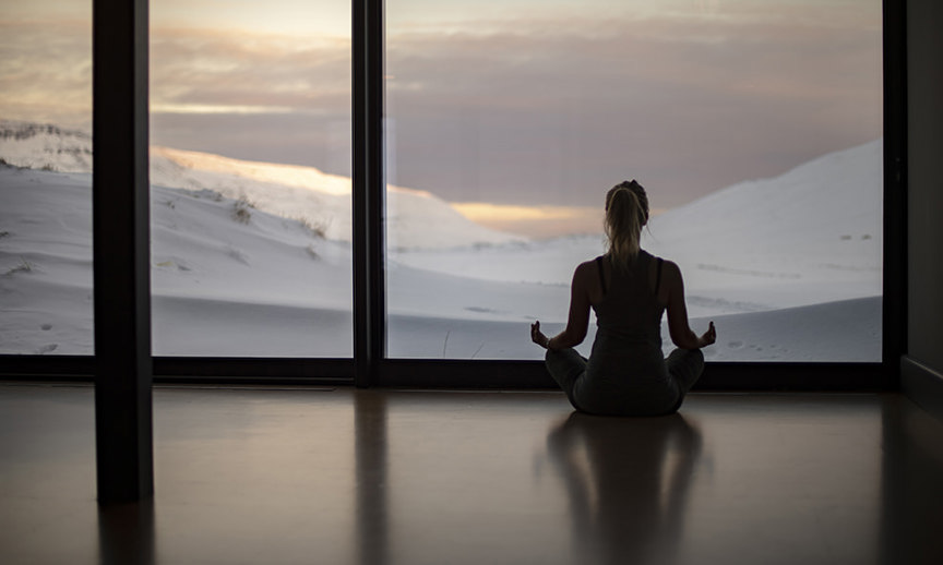 a person does yoga while looking out a window at the Icelandic landscape